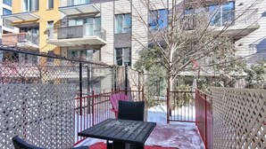 Een balkon met een tafel en stoelen, omgeven door een metalen hek, met een gebouw op de achtergrond.