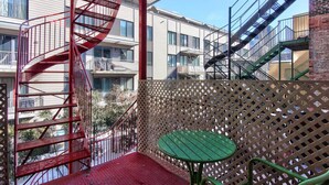 Ein Balkon mit einer roten Wendeltreppe, einem grünen Tisch und einem Gitterzaun.