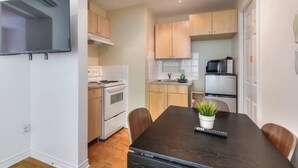 A compact kitchen with white appliances, a dark wooden dining table, and a potted plant.