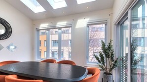 Un comedor moderno con una mesa redonda y sillas naranjas, ventanas amplias y una planta en maceta.