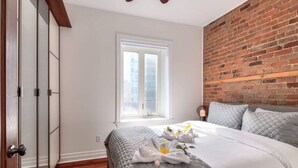 Un dormitorio con pared de ladrillo, un ventanal grande y una cama con manta acolchada y toallas.