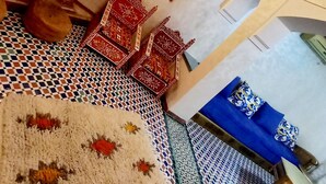 Una habitación con piso estampado, un armario de madera, una silla roja, una mesa azul y un espejo fijado a la pared.