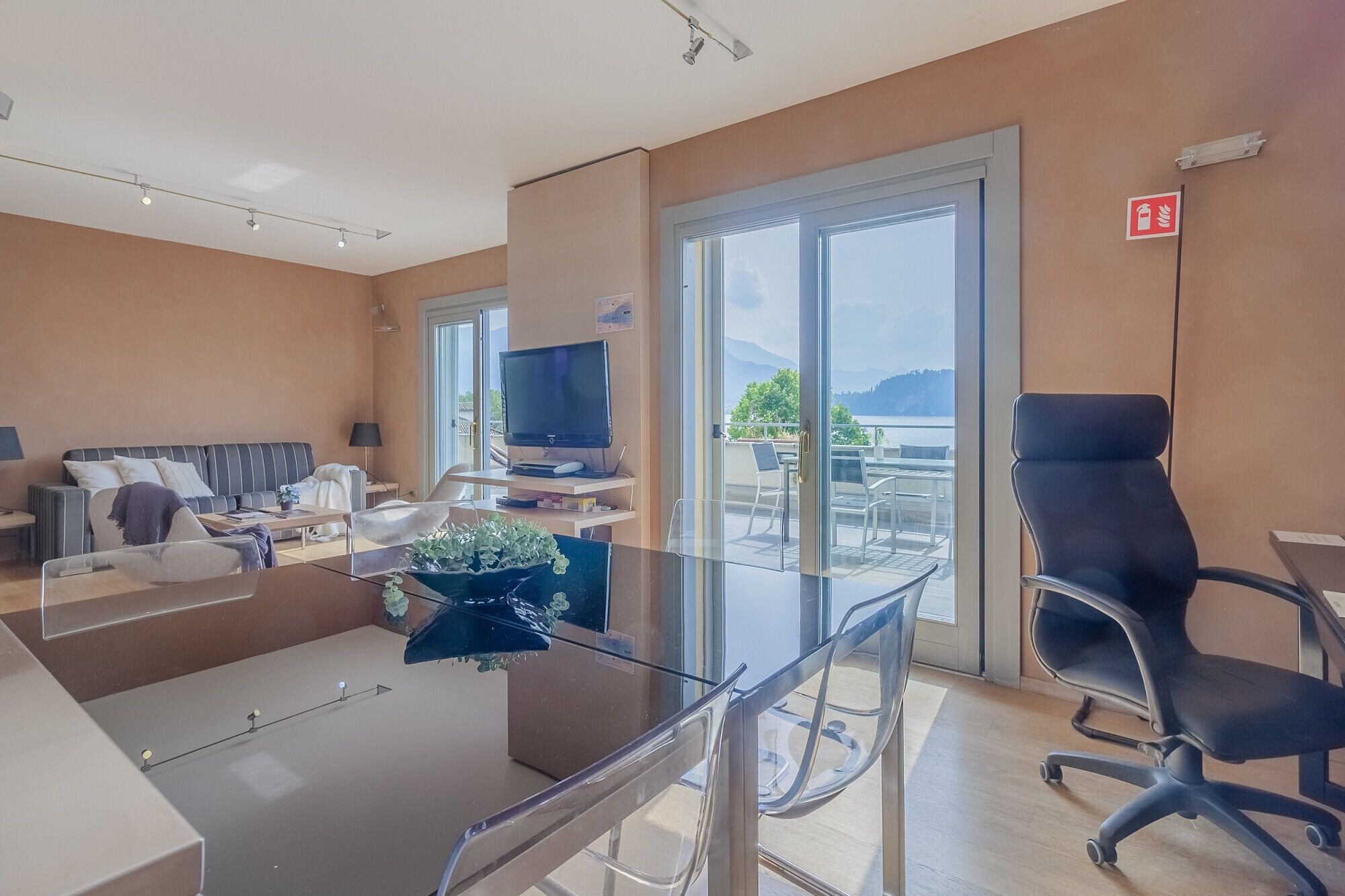 Ett modernt hotellrum med en soffa, TV, ett glasbord, stolar och en balkong med utsikt.