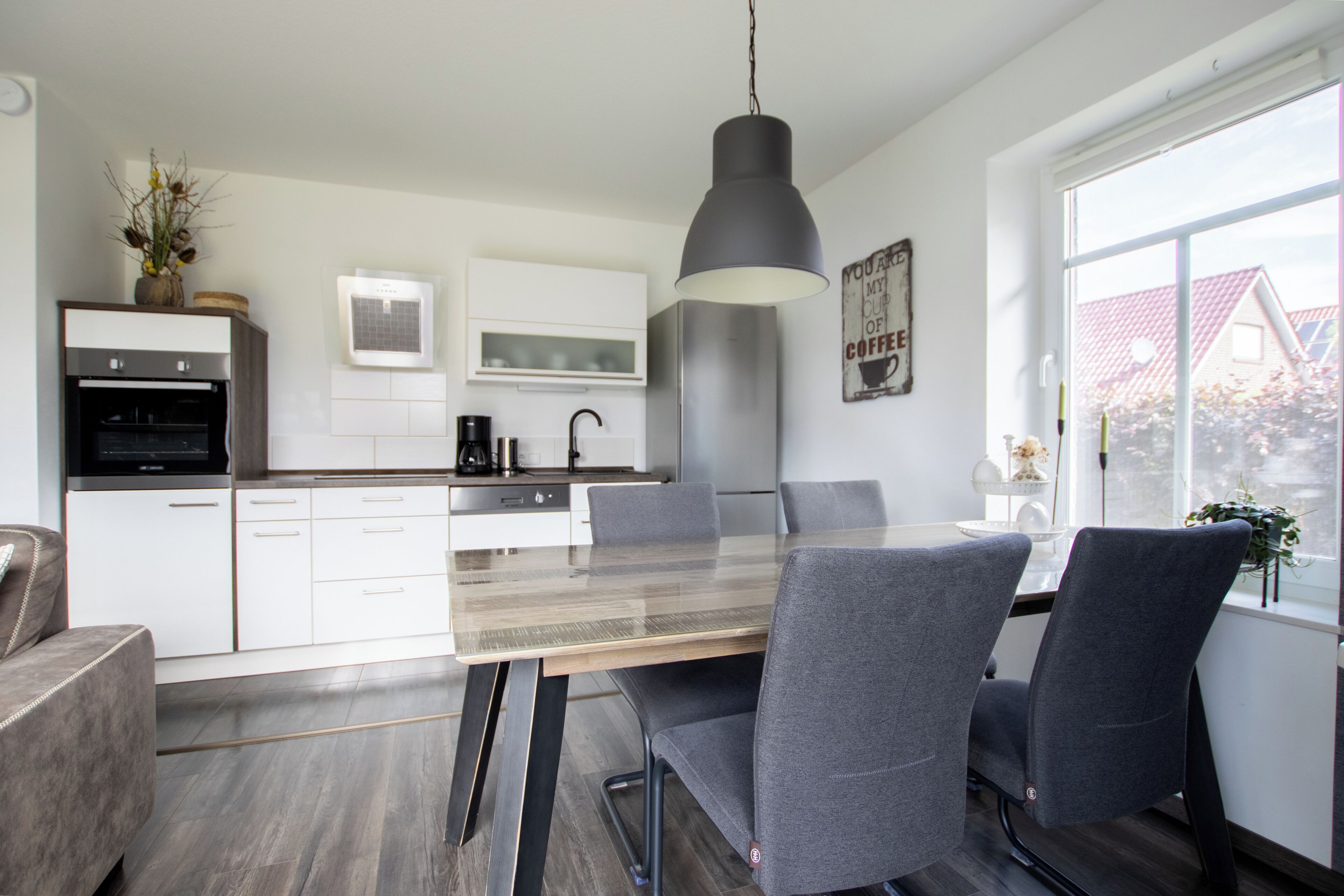 A modern kitchen with white cabinetry, a wooden dining table, and grey chairs.