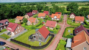 Vista aérea de uma área residencial com casas e telhados vermelhos, cercada por gramados verdes e árvores.