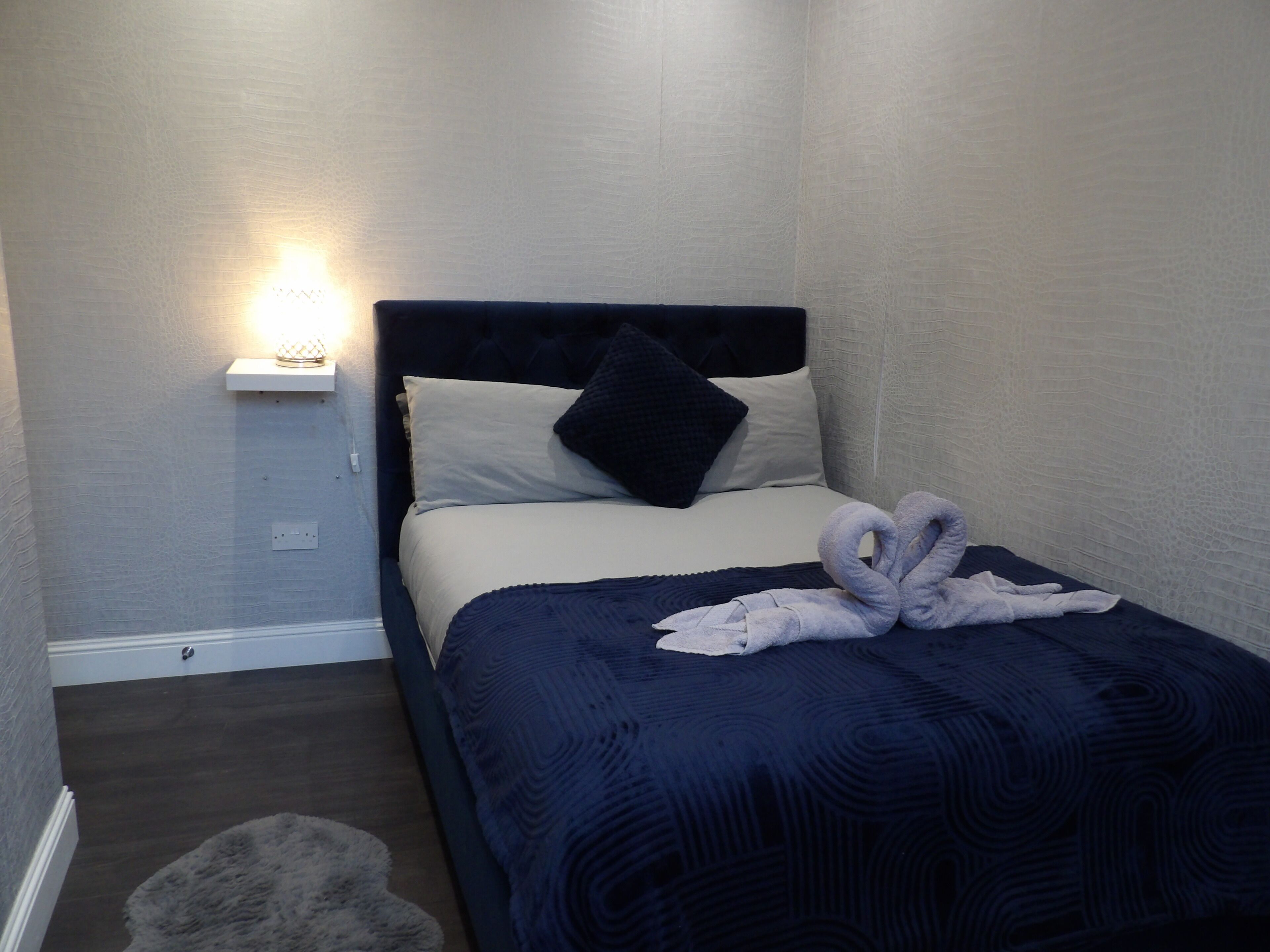 A neatly made bed with a dark blue blanket and a decorative towel arrangement.