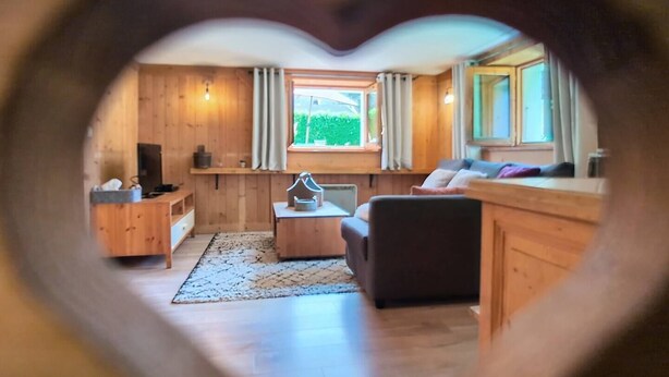 A cozy living room with wooden walls, a sofa, a coffee table, and a window with curtains. - The cosy refuge (Chamonix-Mont-Blanc)