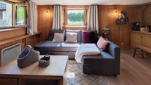 A cozy cabin interior with a wooden interior, a sofa with cushions, a table with a basket, and a window with curtains. - The cosy refuge (Chamonix-Mont-Blanc)