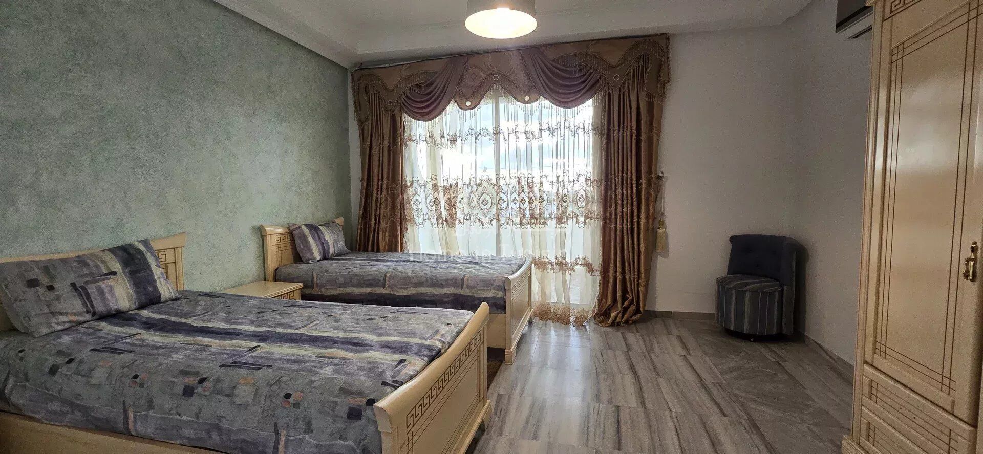 A room with two beds, a wardrobe, and a window with curtains.