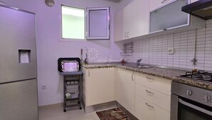A compact kitchen with a refrigerator, a sink, a stove, and a small window.