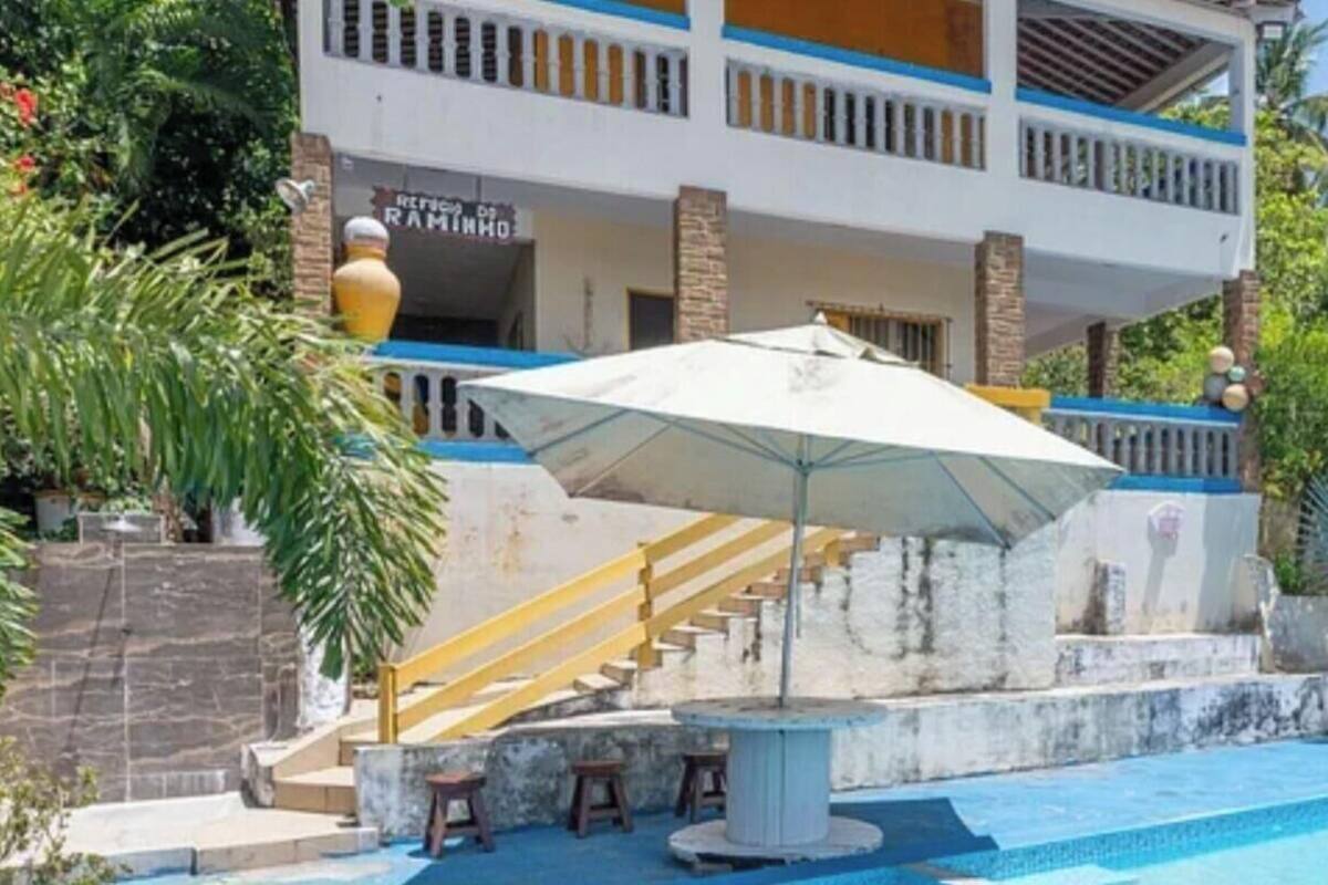 A pool area with a staircase leading to a balcony, surrounded by lush greenery and palm trees.