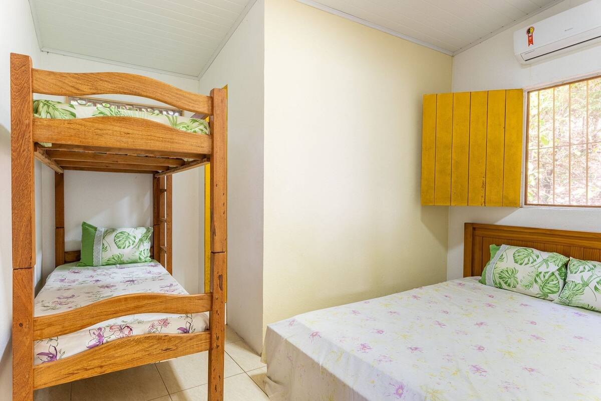 A room with a bunk bed and a single bed, both with floral bedding. There is a yellow cabinet and a window with bars.