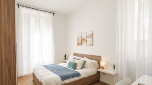 A neatly arranged bedroom with a wooden bed, white bedding, a bedside table with a lamp, and a small potted plant. - Vatican Domvs, 250 meters from the Vatican Museums (Roma)