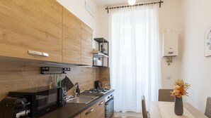 A modern kitchen with wooden cabinets, a black countertop, a coffee machine, and a dining area with a table and chairs. - Vatican Domvs, 250 meters from the Vatican Museums (Roma)