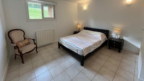 Un dormitorio con cama, una silla, dos mesitas de noche con lámparas, un radiador y una ventana con vistas a zonas verdes.