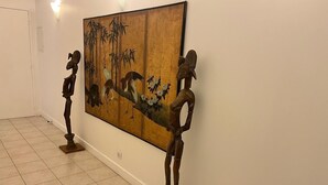 Un pasillo con un cuadro grande y dos esculturas de madera sobre pedestales.