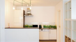 A modern kitchen with white cabinetry, a stainless steel range hood, a microwave, and a dishwasher. - Cozy apartment+kitchen+Netflix (Essen)