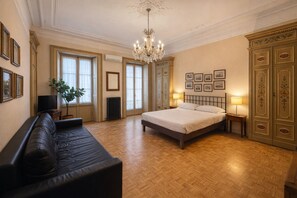 Une chambre spacieuse avec un grand lit, un coin salon avec un canapé, un lustre et une vue sur la ville.