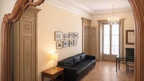 A room with a black leather sofa, a wooden side table with a lamp, a dining table with chairs, and framed pictures on the wall. - dHomes -Apartments Rooms- Galleria Gold  (Milan)