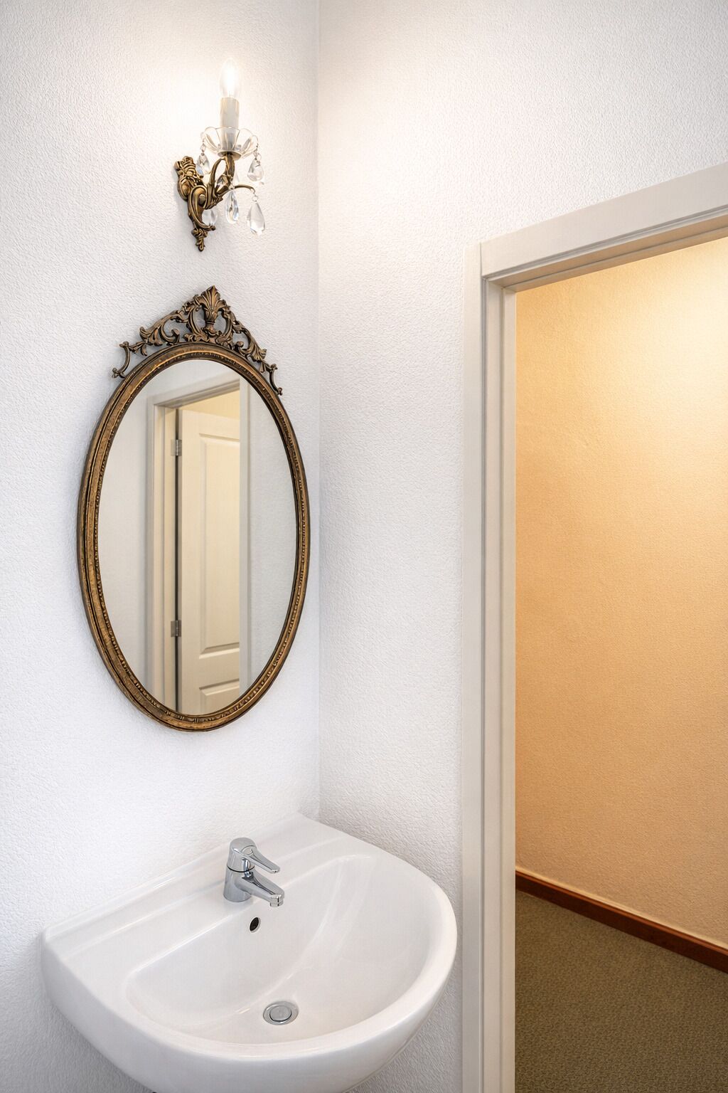 A bathroom with a white sink, a gold-framed mirror, and a wall-mounted light fixture.