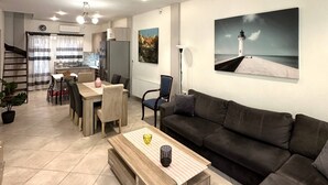 Ein modernes Wohnzimmer mit Sofa, Couchtisch und Essbereich. An der Wand hängt ein Gemälde eines Leuchtturms.