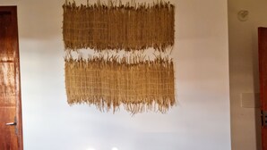Una cama bien hecha con sábanas blancas y una manta verde, un tapiz tejido encima, y una puerta de madera a la izquierda.