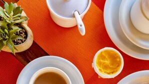 Una mesa con una taza de café, un plato con una porción de fruta y un tazón pequeño de salsa amarilla.