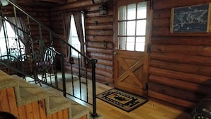 A wooden cabin interior with a staircase, a door with a window, and a rug on the floor. - Authentic Log Cabin in the Southern Ozark Mountains with hot tub (Mountain Home)