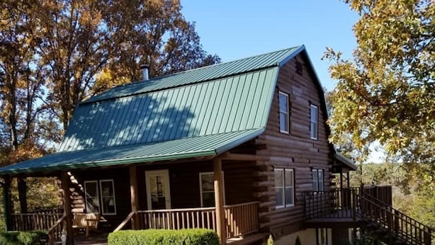 A log cabin with a green metal roof, a porch, and a staircase leading to a deck. - Authentic Log Cabin in the Southern Ozark Mountains with hot tub (Mountain Home)