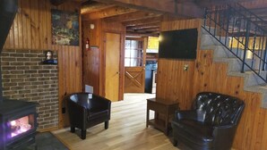 A cozy cabin interior with a fireplace, leather chairs, a television mounted on the wall, and a wooden staircase. - Authentic Log Cabin in the Southern Ozark Mountains with hot tub (Mountain Home)