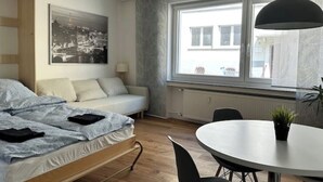 Une chambre à coucher de taille modeste, comprenant un lit, un canapé, une table à manger et une grande fenêtre.