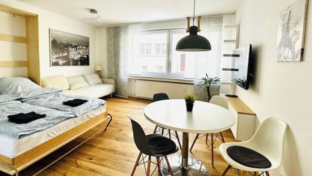Une chambre moderne avec un lit, une table à manger et des chaises. Une fenêtre offre une vue sur les bâtiments environnants.