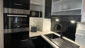 Une cuisine moderne avec des meubles de rangement noirs, un four en acier inoxydable, un four à micro-ondes et un évier avec un robinet.