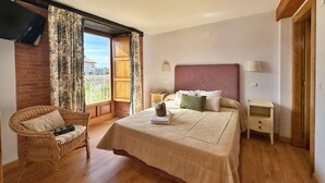A bedroom with a large bed, a wicker chair, a nightstand, and a TV mounted on the wall. - 🏡 Perfect Island Getaway - Townhouse with Private Parking 🚗✨. (Isla)