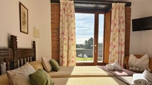 Habitación de hotel con dos camas, cabecera de madera, ventana con cortinas florales y vista a una cancha de tenis.