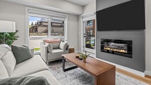 Una sala de estar moderna con chimenea, un sofá, una mesa de centro y vistas a un edificio a través de grandes ventanales.