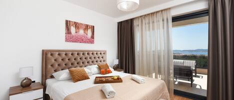 A modern hotel room with a large bed, a nightstand, a tray with fruit, and a view of the outdoors.