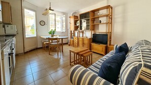 Ett kompakt bostadsutrymme med ett litet kök, en matplats och en soffa med randiga kuddar.