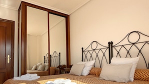 A neatly made bed with a patterned bedspread, a large mirror, and a wooden door. - Cozy Tourist Apartment in Somo, Ideal for Families. (Somo)