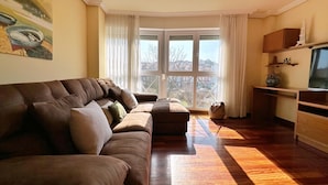 A living room with a brown sofa, a wooden coffee table, and a TV stand. - Cozy Tourist Apartment in Somo, Ideal for Families. (Somo)