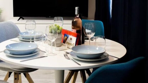 A dining area with a table set for two, a bottle of wine, and a menu. A television in the background displays the Netflix logo. - Modern 2-room apartment | 6 persons | WIFI (Unknown)