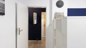 A hallway with a wooden floor, a white door, a black wall with a round mirror, and a clock. - Modern 2-room apartment | 6 persons | WIFI (Unknown)
