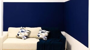 A corner room with a white sofa and two patterned pillows, a dark blue accent wall, and a wooden floor. - Modern 2-room apartment | 6 persons | WIFI (Unknown)