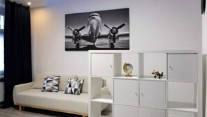 A modern living room with a sofa, a white cabinet, and a black and white airplane painting on the wall. - Modern 2-room apartment | 6 persons | WIFI (Unknown)