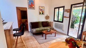 Ein gemütlicher Wohnbereich mit einer Couch, einem Couchtisch und Sesseln. Ein Esstisch mit einem Blumenstrauß steht ebenfalls dort. Das Zimmer verfügt über Holzbalken an der Decke und einen Blick durch eine Glastür.