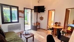 Ein gemütliches Wohnzimmer mit einer Couch, einem Couchtisch und einem Essbereich mit Stühlen und einem Tisch. An der Wand ist ein Fernseher angebracht und ein Fenster lässt natürliches Licht herein.