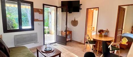 Una sala de estar acogedora con sofá, una mesa de centro y un comedor con sillas y mesa. Hay un televisor montado en la pared y una ventana que proporciona luz natural.