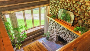 A stone fireplace with a wooden mantel, a large window with curtains, and potted plants. - The Little Place on Pine (Harrison)