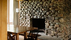 A stone fireplace with a wooden mantel and a table with chairs in front. - The Little Place on Pine (Harrison)