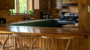 A rustic wooden kitchen with a bar area, wooden chairs, and a window providing natural light. - The Little Place on Pine (Harrison)